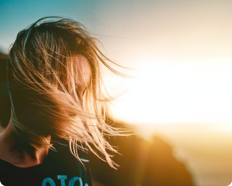 A photograph close-up of a blonde woman looking down but being covered by her hair in the wind to demonstrate feelings of isolation and loneliness.