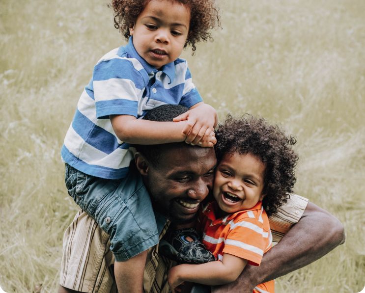 A picture of a man carrying two boys, one on his shoulder and the other in his arms.